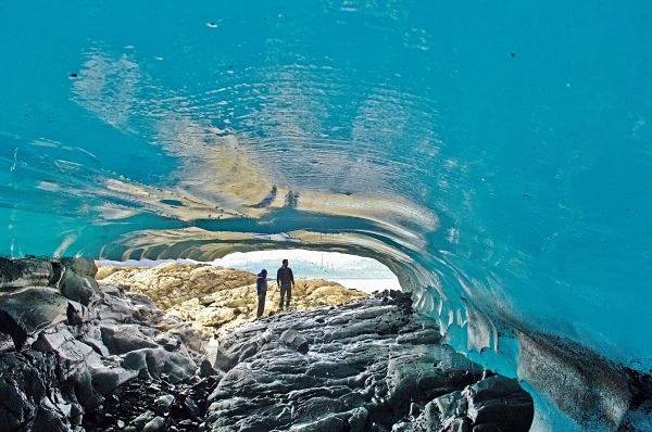 Cueva de hielo azul con dos personas en entrada bajo agua