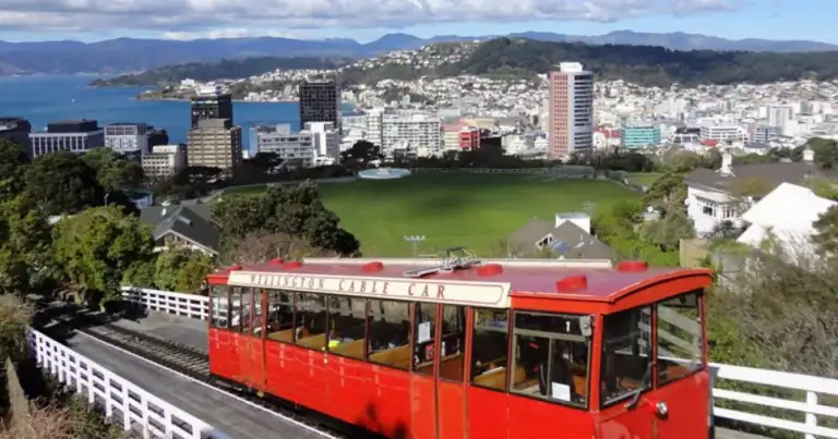 Vista aérea de ciudad costera con bahía azul y tranvía rojo