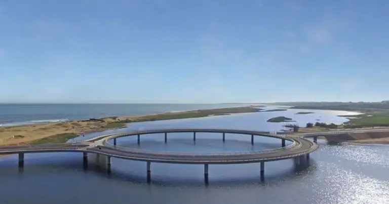 Puente circular sobre agua en paisaje costero y llano
