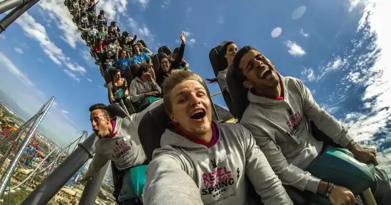 Personas en montaña rusa con brazos levantados en parque temático