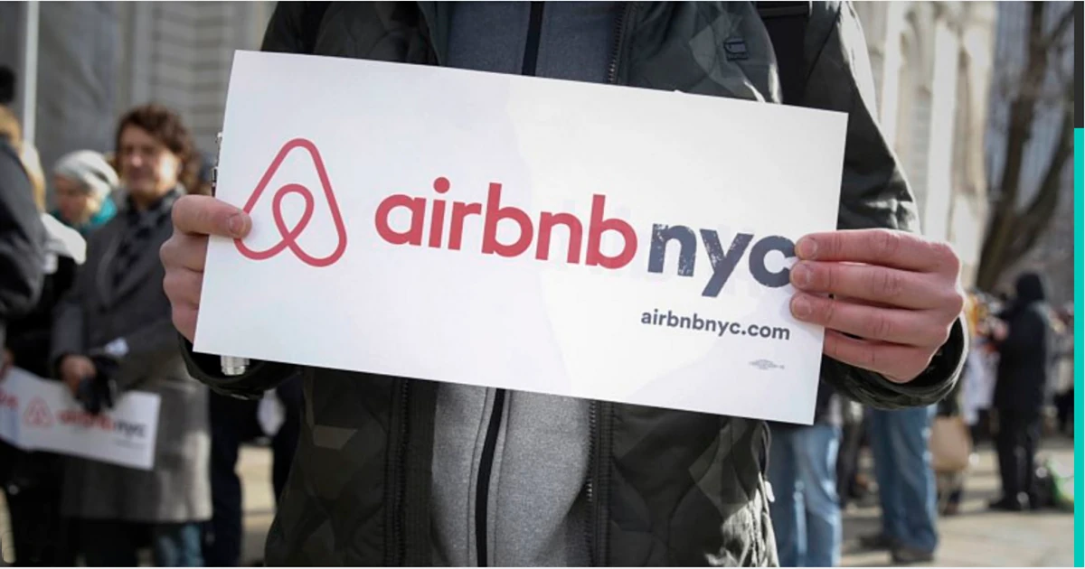 Persona mostrando cartel de Airbnb NYC con logo