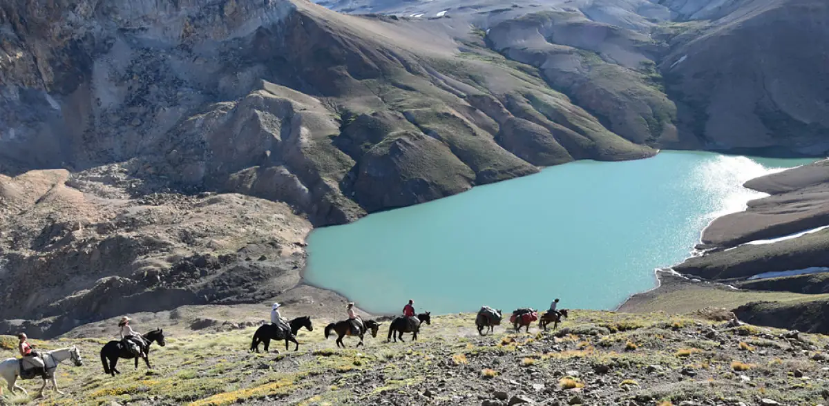 Grupo de personas cabalgando ante glaciar y laguna turquesa