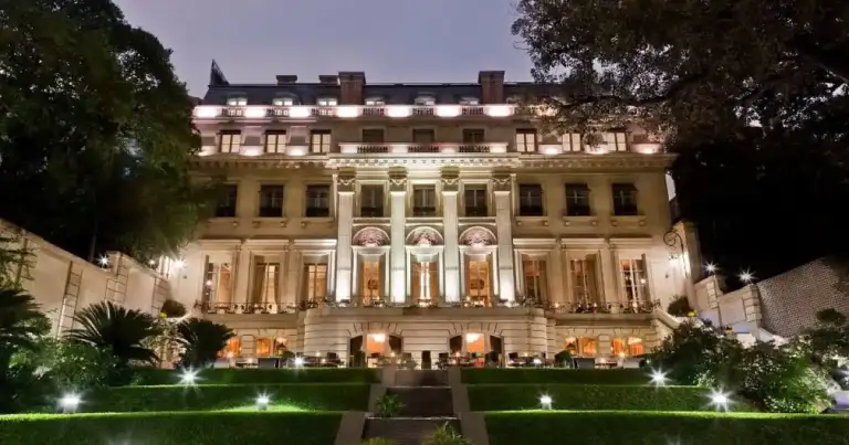 Edificio histórico de dos pisos iluminado de noche con jardín