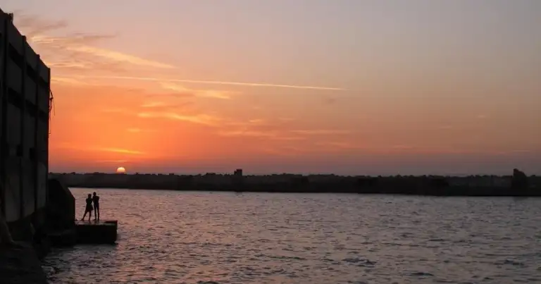 Atardecer anaranjado sobre río o bahía con silueta de estructura