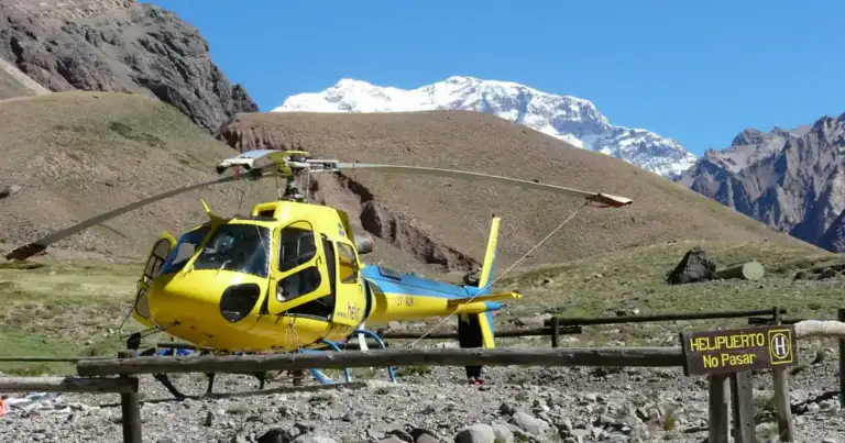 Helicóptero amarillo en base de rescate con montaña nevada al fondo