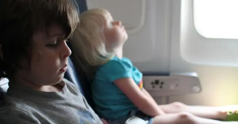 Dos niños en asiento de avión, uno mirando por la ventana