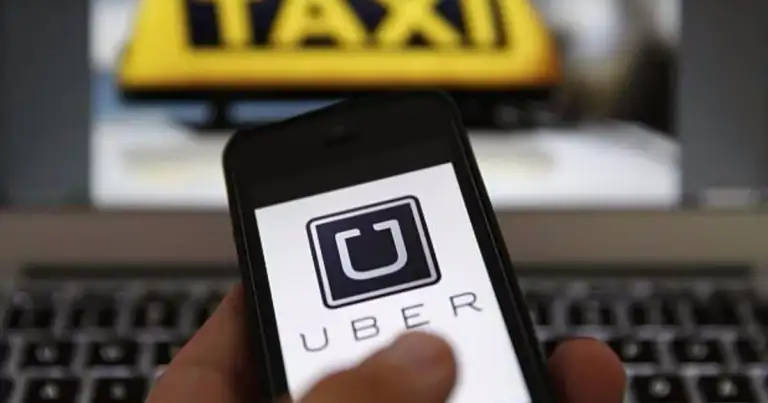 Mano sosteniendo smartphone con aplicación Uber en pantalla, taxi al fondo
