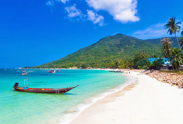 Playa de arena blanca y aguas turquesas en Tailandia con barca tradicional y palmeras