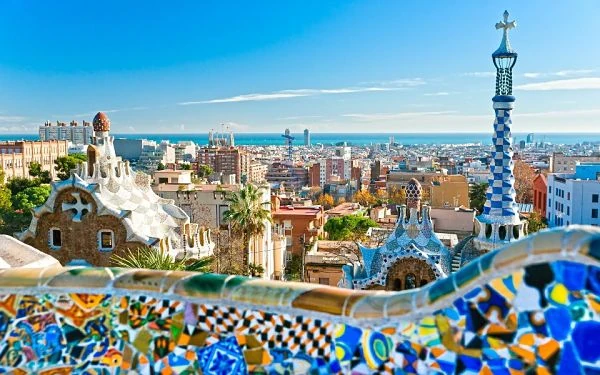 Vista panorámica del Park Güell de Barcelona, con sus coloridos mosaicos modernistas, arquitectura de Gaudí y la ciudad extendiéndose hacia el mar Mediterráneo.
