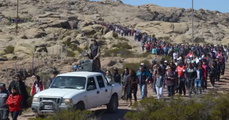 Gran multitud en montaña rocosa esperando junto a vehículo blanco