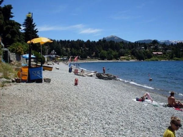 Playa de grava con bañistas y montaña nevada al fondo
