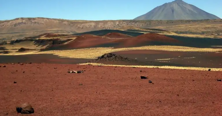 Volcán cónico sobre llanura con cerros de lava de colores variados
