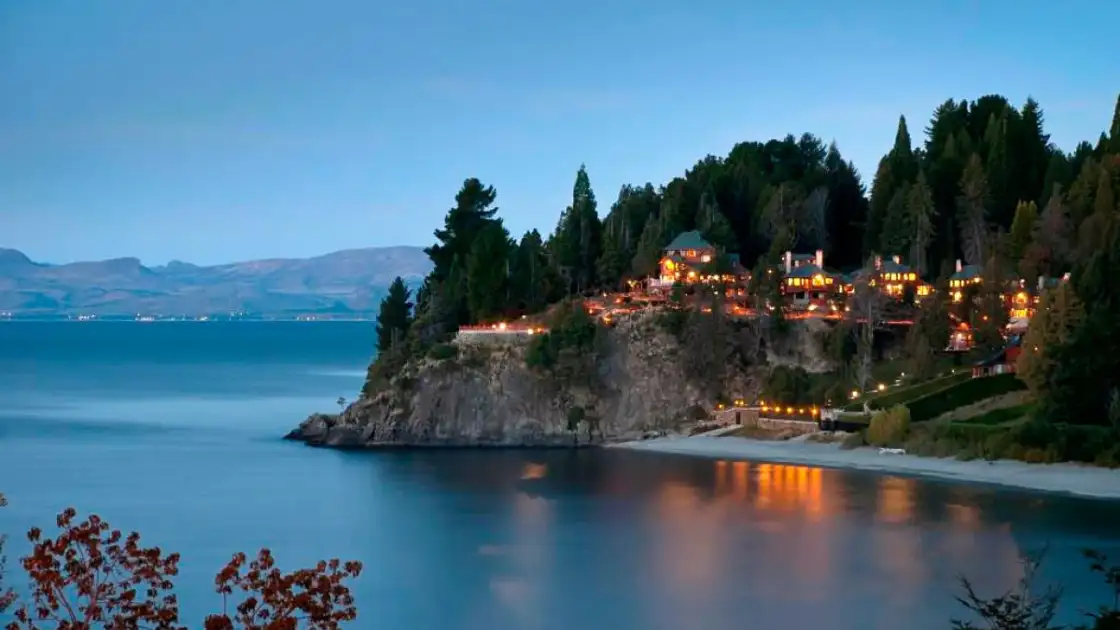 Lago en el atardecer con árboles en la orilla y luces reflejadas