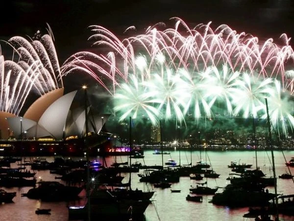 Fuegos artificiales iluminan la Ópera de Sídney reflejados en puerto nocturno