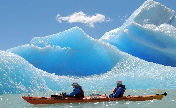 Dos personas en kayak azul frente a iceberg azul turquesa de gran tamaño