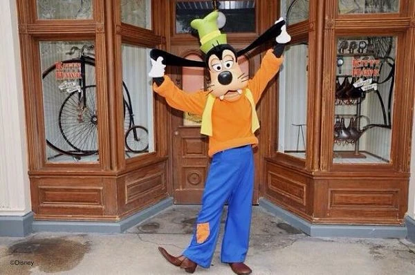 Personaje de Disney en uniforme amarillo frente a puertas de madera