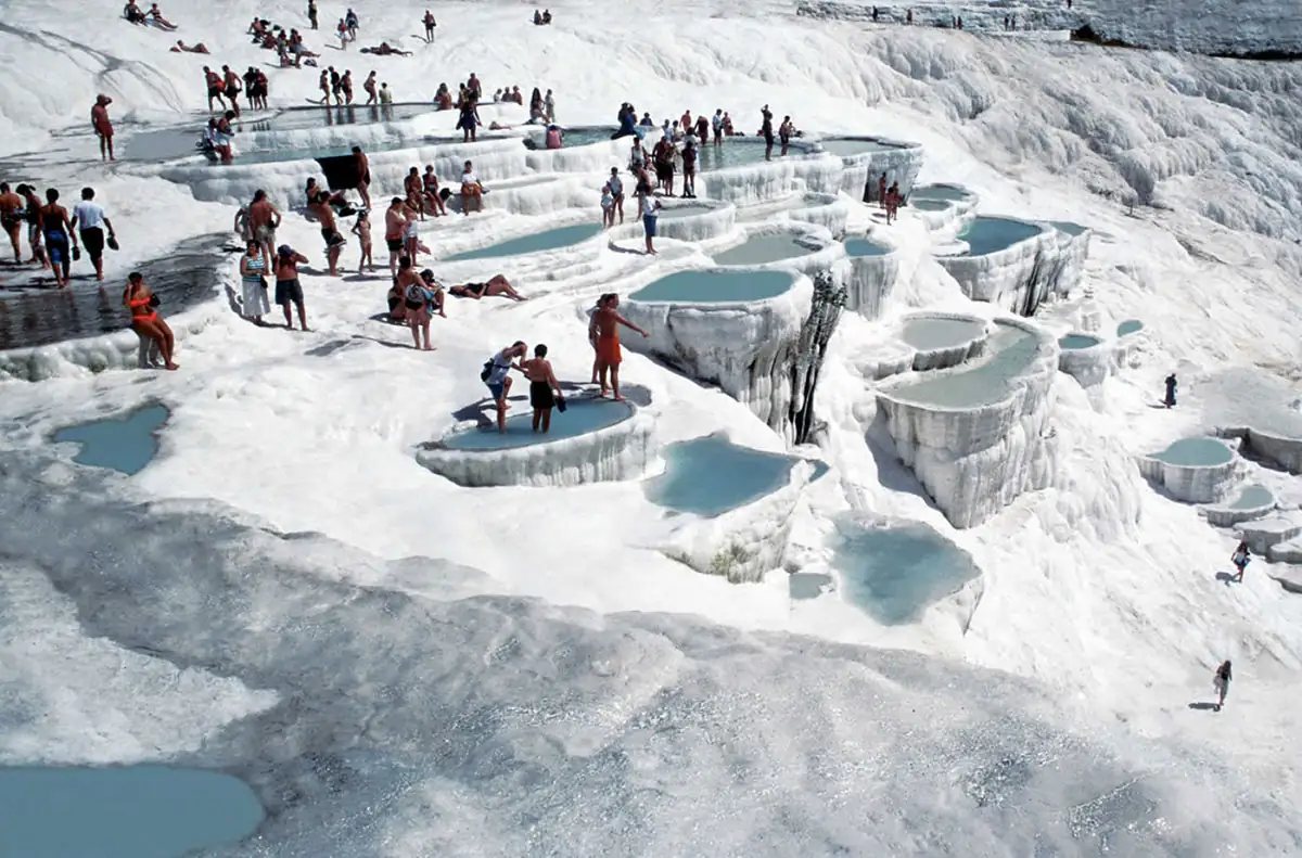 Turistas en terrazas de travertino blanco con aguas termales