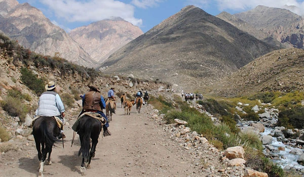 Excursionistas a caballo en sendero montañoso con arroyo