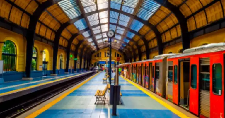Interior de estación de tren con tren rojo en andén y estructura de arcos