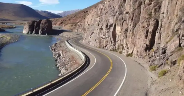 Carretera serpenteante junto a acantilado rocoso y río de aguas turquesas