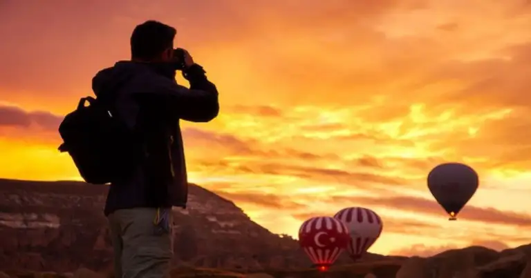 Persona fotografiando al atardecer con globos aerostáticos en el horizonte