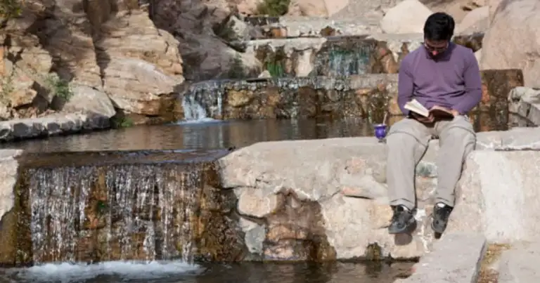 Mujer leyendo junto a aguas termales entre rocas y vegetación