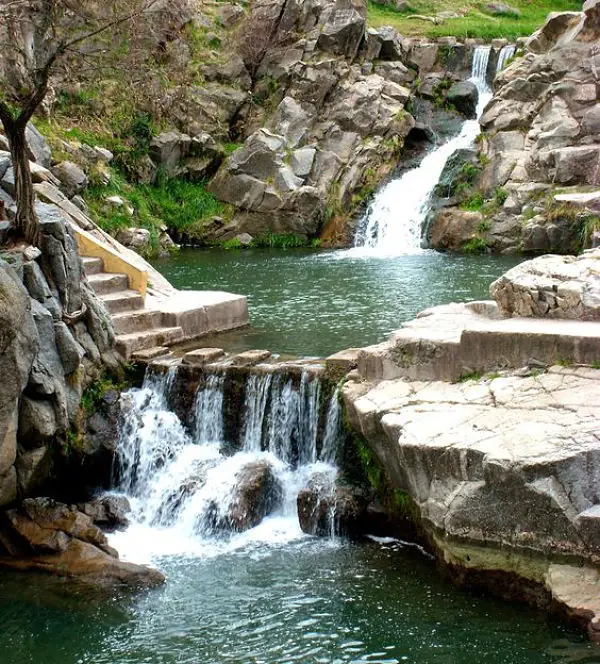 Cascada natural en roca con piscina de agua verde y árboles altos