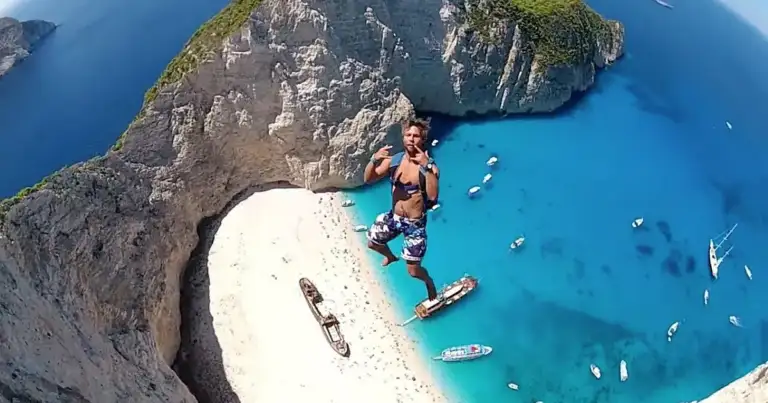 Persona saltando desde acantilado hacia agua azul turquesa cristalina