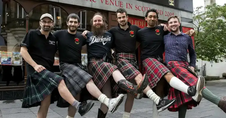 Grupo de hombres levantando kilts escoceses frente a un pub