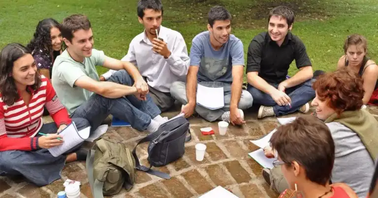 grupo de jovenes sentados en el cesped escribiendo y leyendo