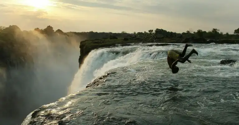 Persona saltando en aguas rápidas junto a cascada