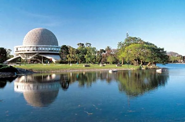 Planetario con cúpula geodésica reflejada en laguna rodeada de árboles