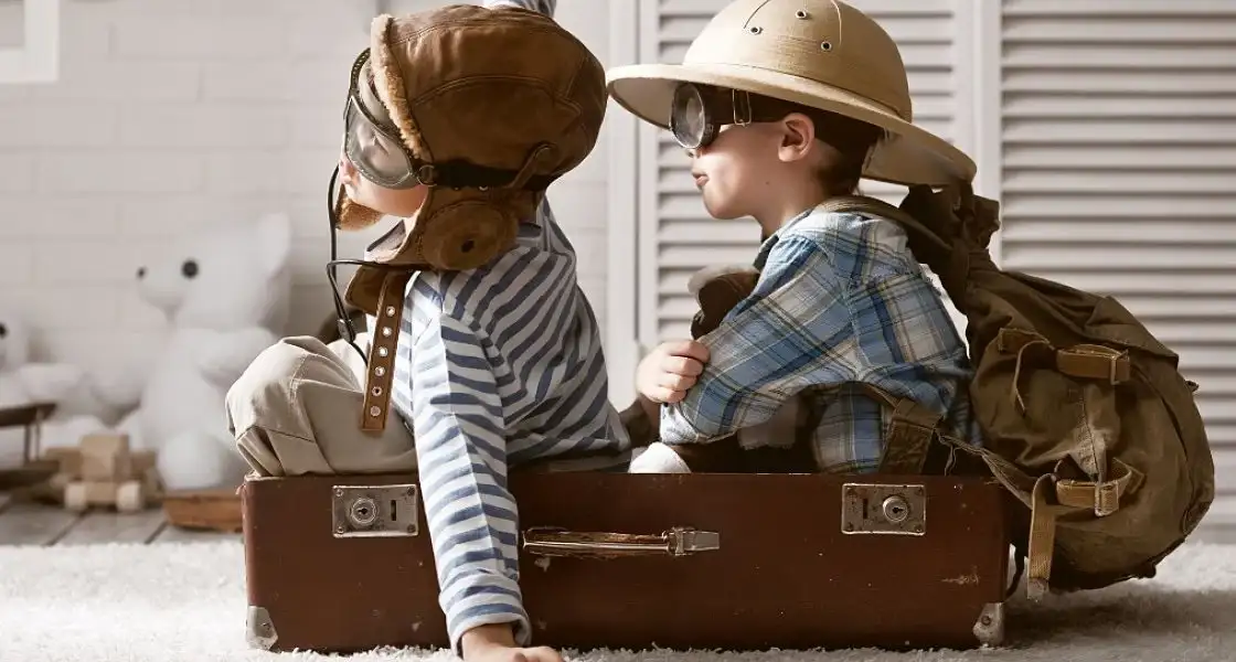 Dos niños con sombreros sentados sobre una maleta vintage