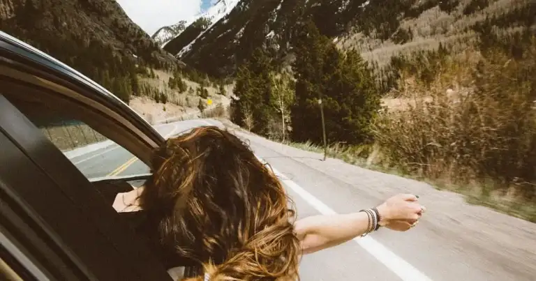 Persona con brazo extendido por ventanilla de auto en ruta montañosa