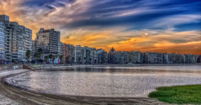 Playa urbana al atardecer con rascacielos de fondo y cielo colorido