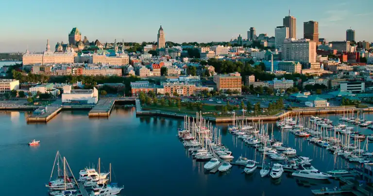 Vista aérea de ciudad portuaria con veleros anclados y rascacielos coloridos