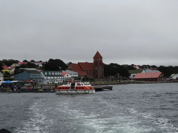Pueblo costero con iglesia de techo rojo, casas coloridas y barco en el agua gris