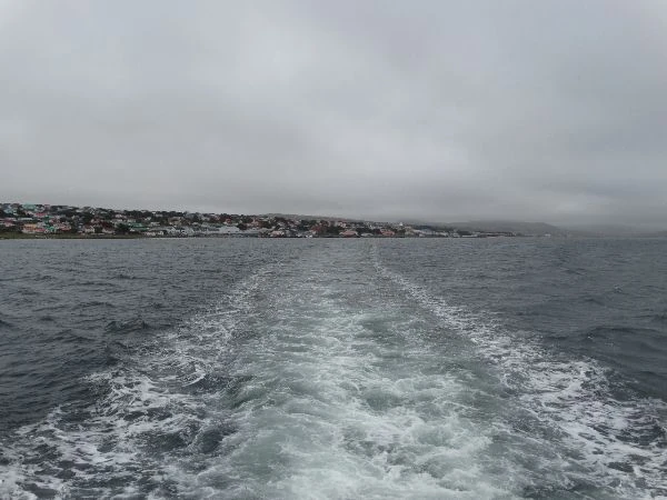 Vista desde un barco que se aleja del puerto, mostrando el pueblo costero en la distancia