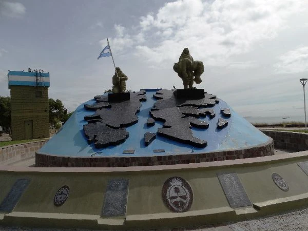 Monumento conmemorativo con estatuas de soldados sobre base azul y objetos militares