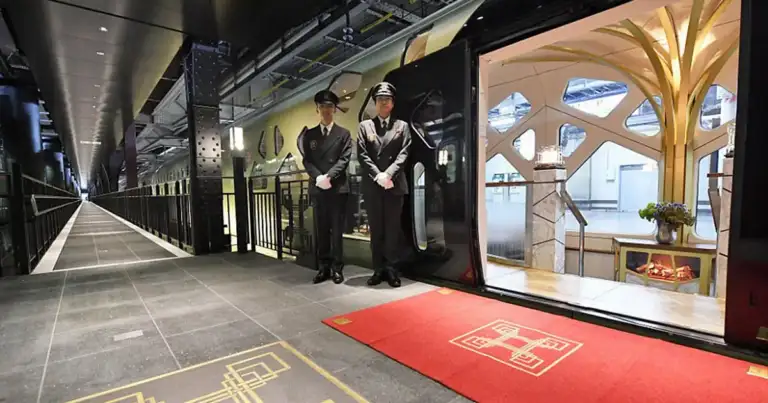 Interior de tren de lujo con personal uniformado y grandes ventanales panorámicos