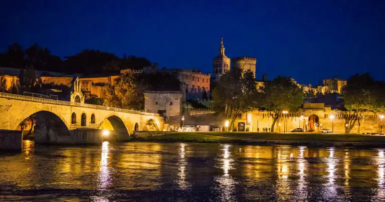 Puente de piedra iluminado sobre río con arquitectura medieval de fondo al atardecer