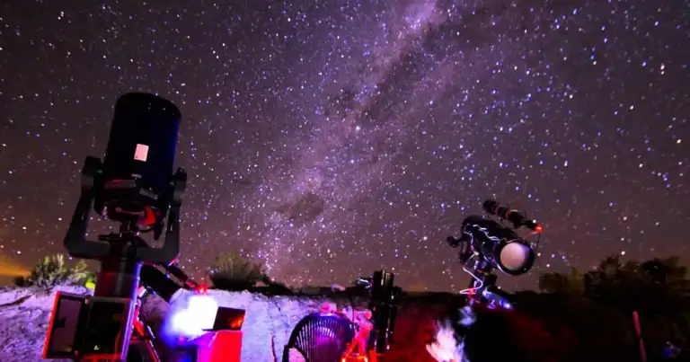 Telescopios iluminados con luces de colores apuntando al cielo nocturno estrellado