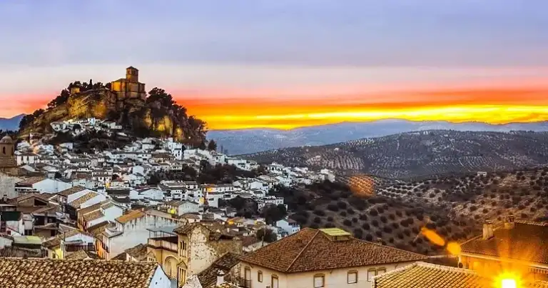 Ciudad blanca con fortaleza de piedra en colina al atardecer