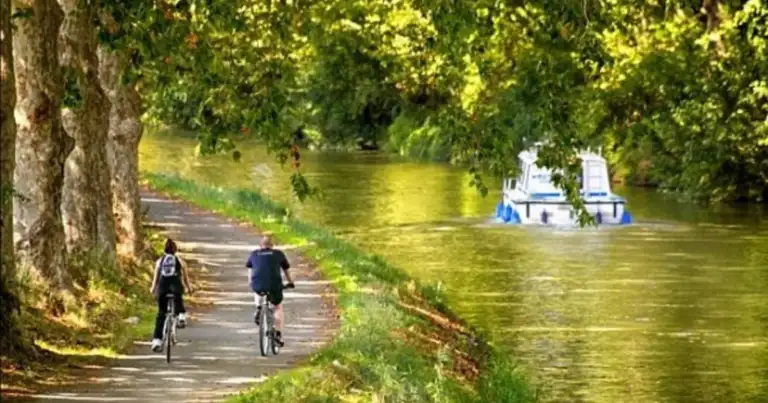 Ciclistas en camino de tierra junto a canal con agua verde y vegetación frondosa