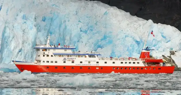 Barco de expedición rojo navegando junto a glaciar azul de hielo