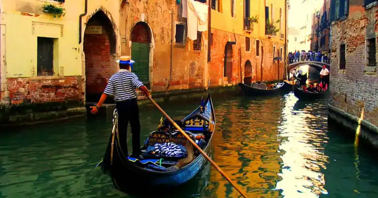 Gondolero en barco azul navegando entre edificios históricos en canal de agua verde
