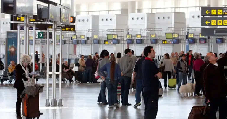 Terminal de aeropuerto concurrida con mostrador de checkin y paneles informativos