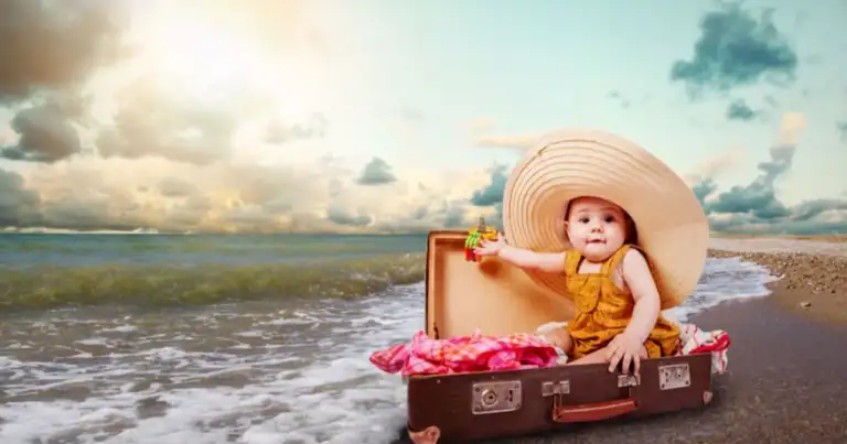 Bebé sentado en maleta de playa con sombrero grande junto a orillas del mar