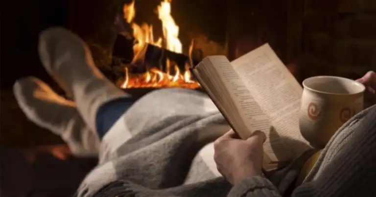 Persona leyendo libro junto a fuego acogedor con taza de café