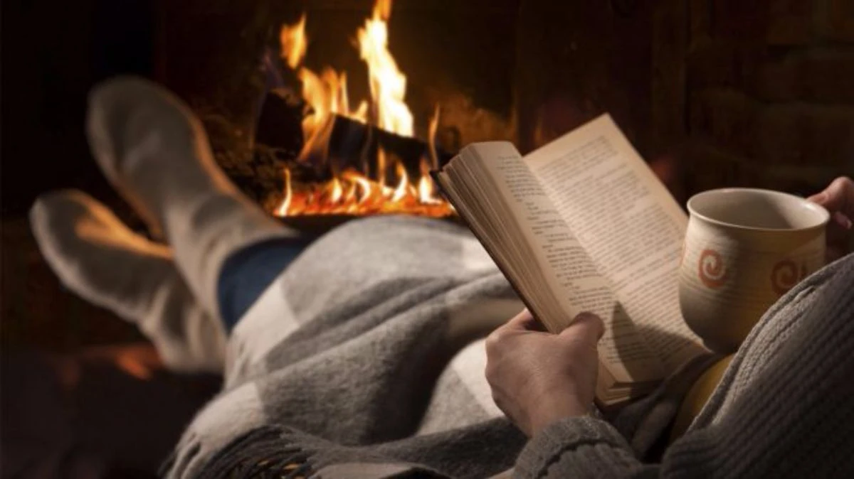 Persona leyendo libro junto a fuego acogedor con taza de café